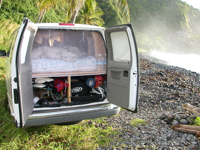 Bed above, four surfboards, a windsurfer, kite board, sails, and a fishing pole beneath.